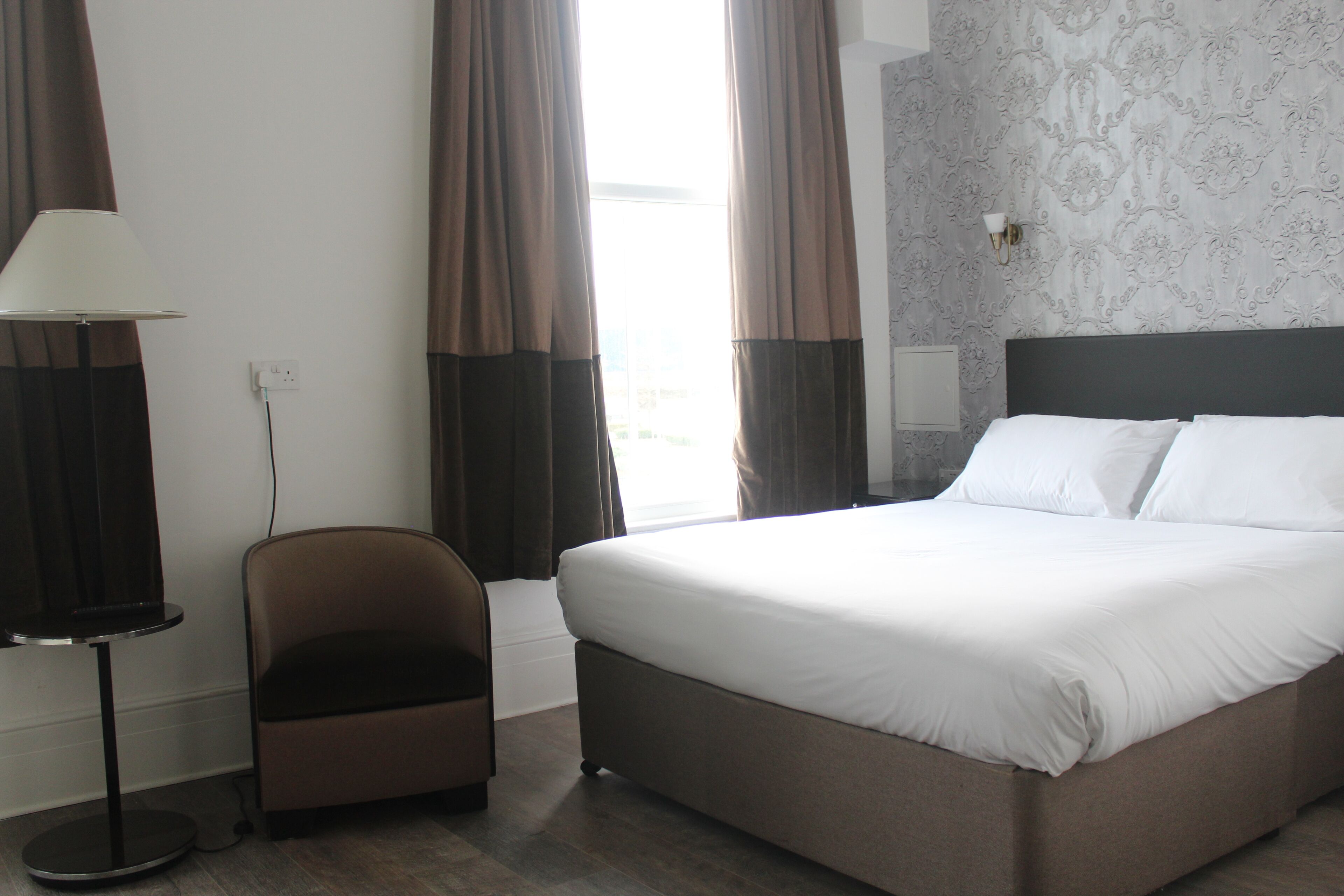 A hotel room with a large bed, a chair, a lamp, and a window with curtains.