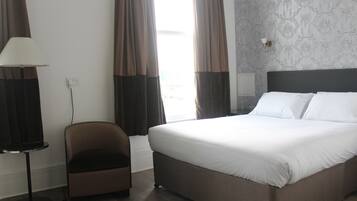 A hotel room with a large bed, a chair, a lamp, and a window with curtains.
