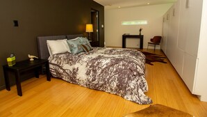 Een moderne slaapkamer met een groot bed, een nachtkastje, een lamp, een stoel en een kledingkast.