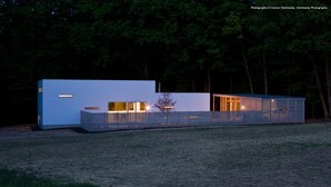Een modern, minimalistisch huis met een plat dak, grote ramen en een goed verlicht interieur.