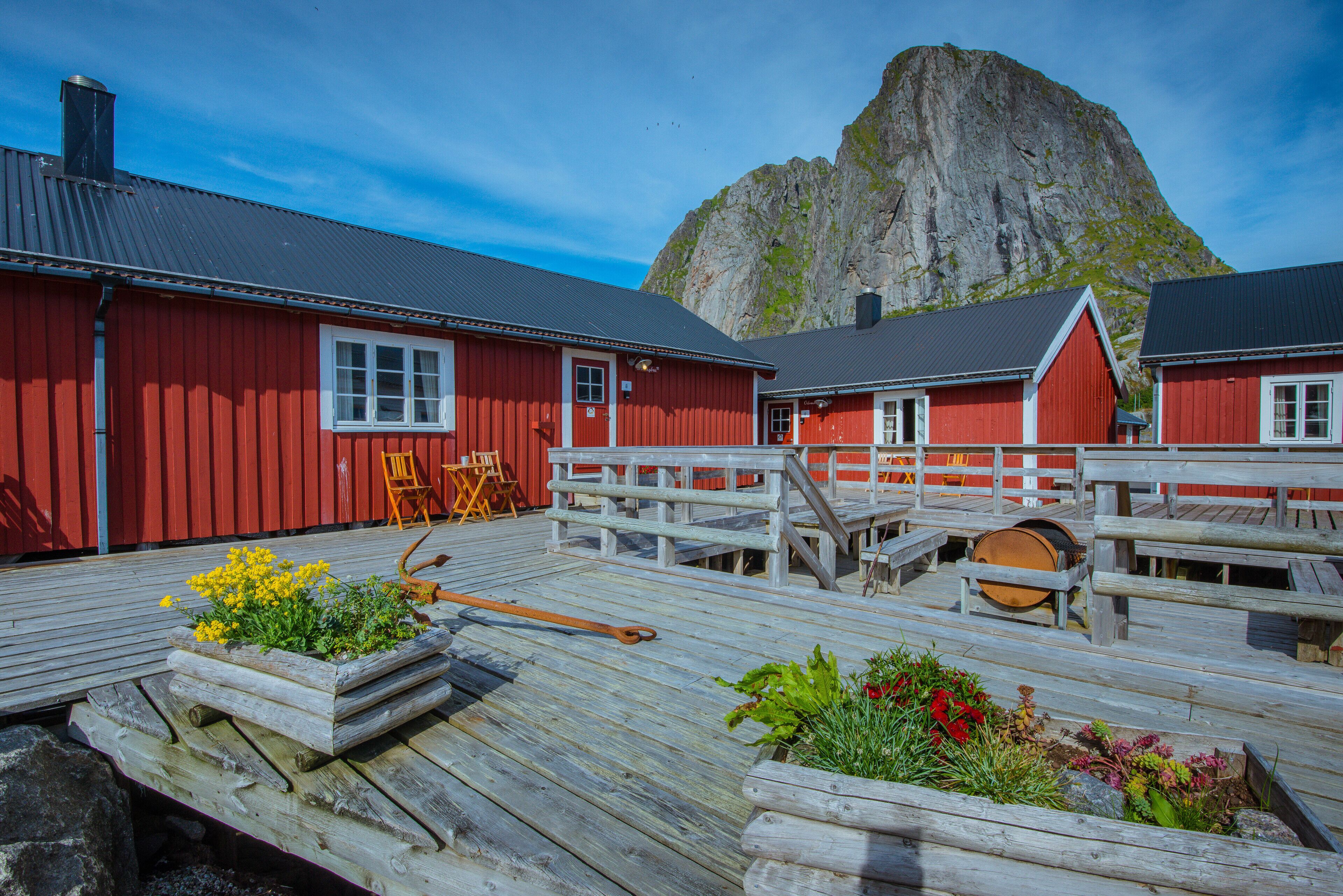 Een houten terras met zitplaatsen buiten, een rood gebouw en een berg op de achtergrond.