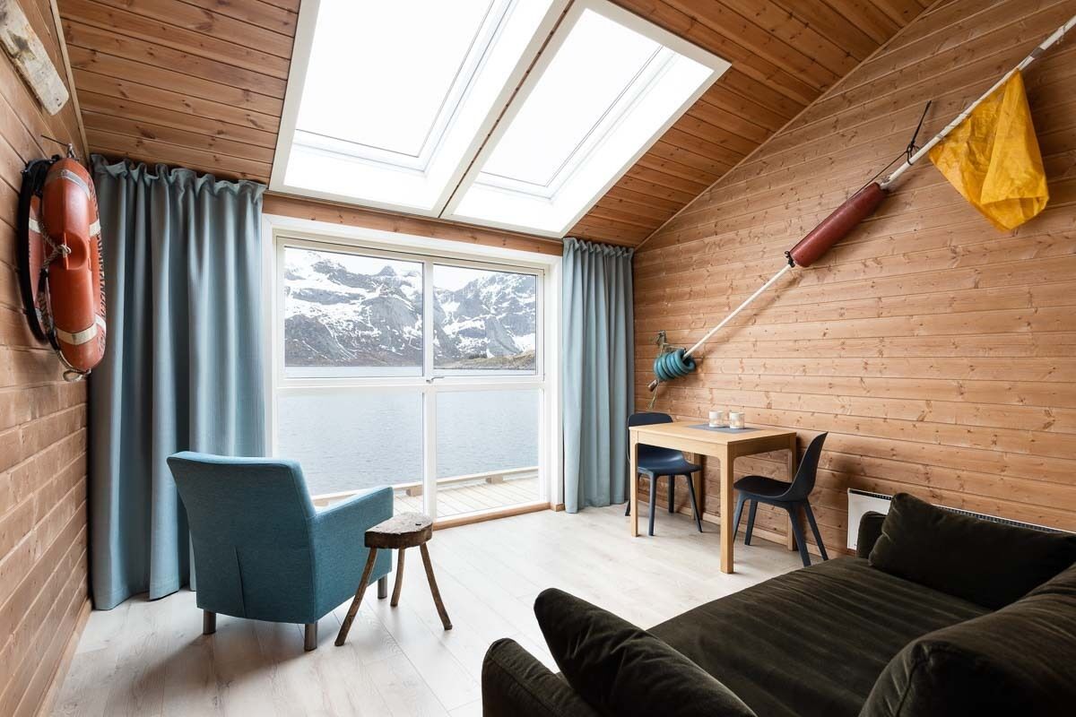 Une pièce chaleureuse aménagée comme une cabane, avec une grande fenêtre, des murs en bois, un canapé, un bureau et une chaise.