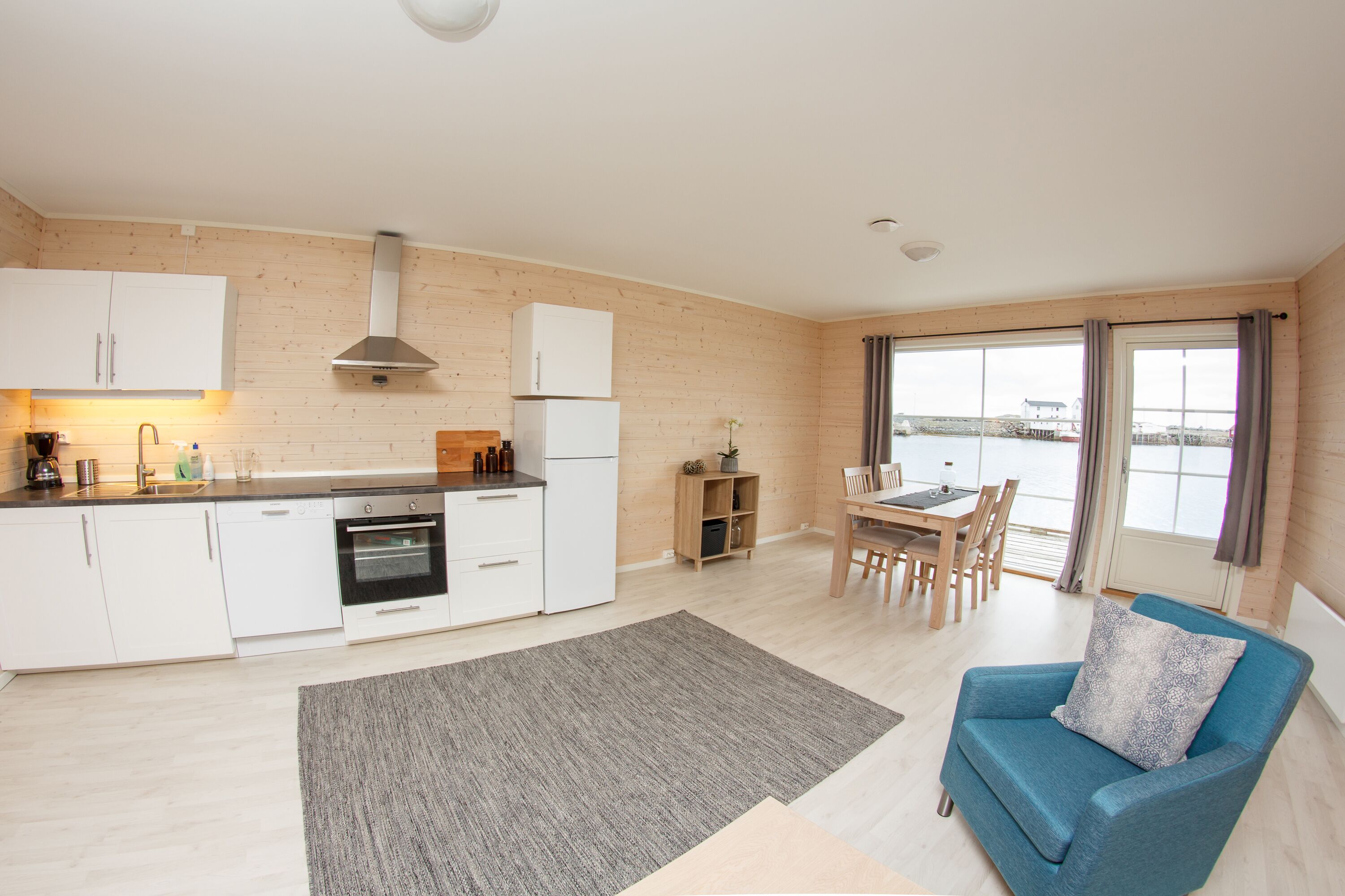 A modern kitchen with white cabinets, a built-in oven, and a dining area with a table and chairs.