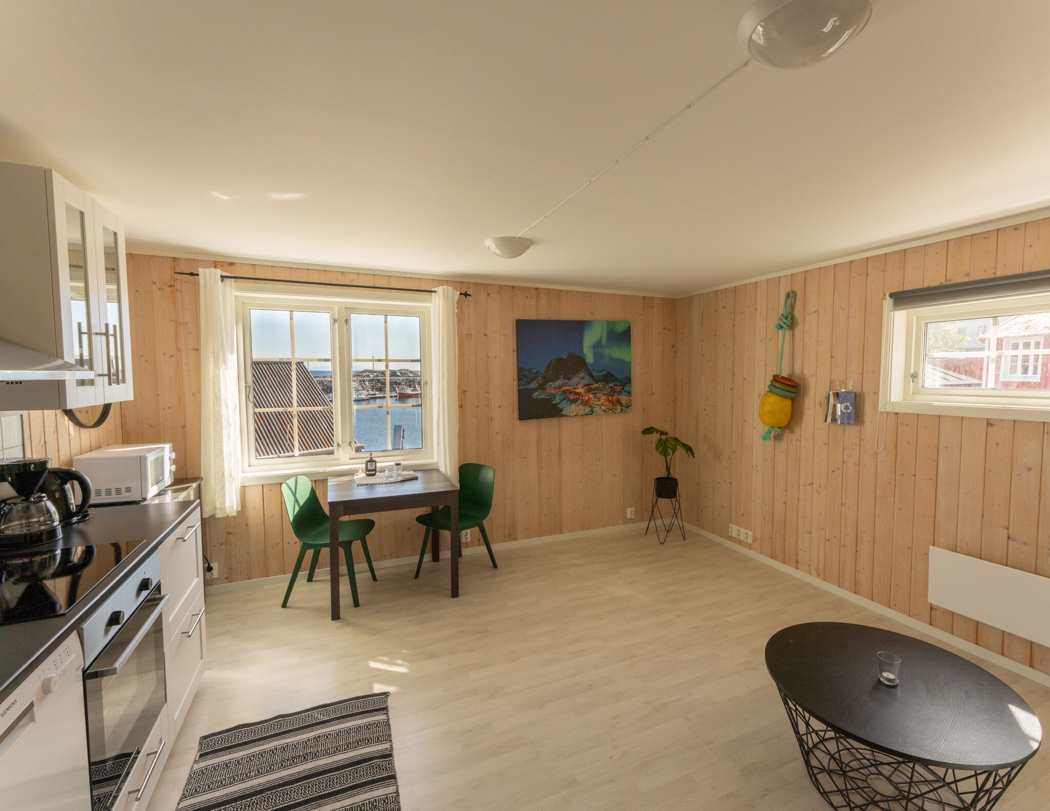 A modern kitchen with a dining area, wooden walls, and a view of a harbor.