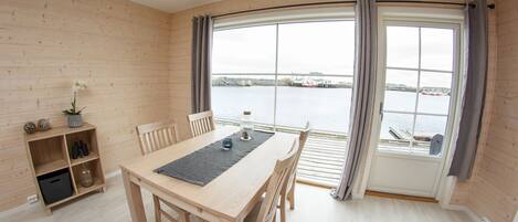 Un comedor de madera con una mesa, sillas y vistas al agua a través de amplios ventanales.