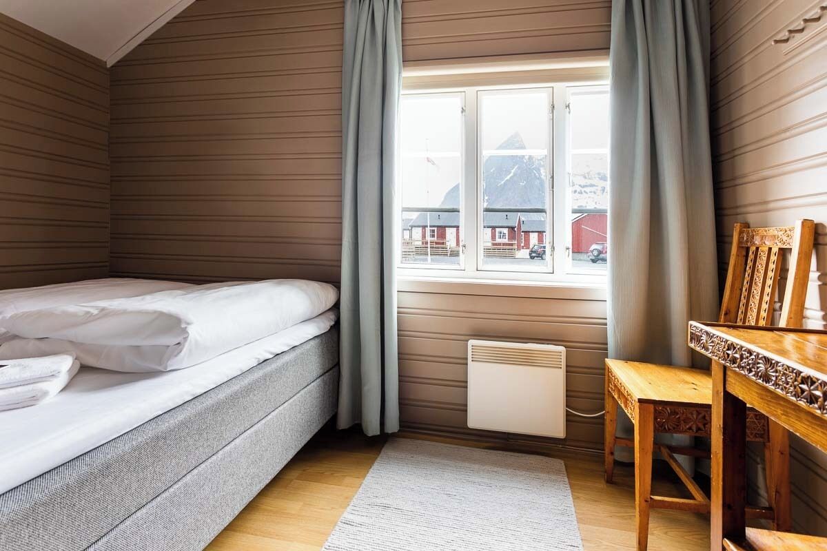 A room with a bed, a wooden table, a window with curtains, and a radiator.
