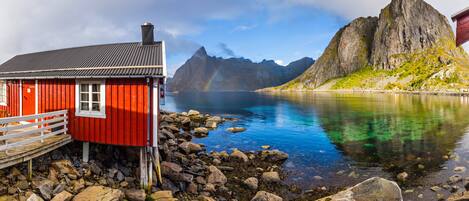 A red wooden building with a dock, a clear lake, and a mountain in the background.