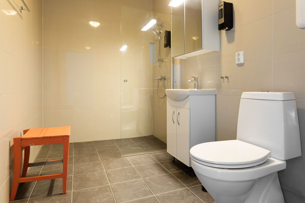 A bathroom with a toilet, sink, and shower. There is a small wooden stool in the corner.