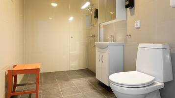 A bathroom with a toilet, sink, and shower. There is a small wooden stool in the corner.