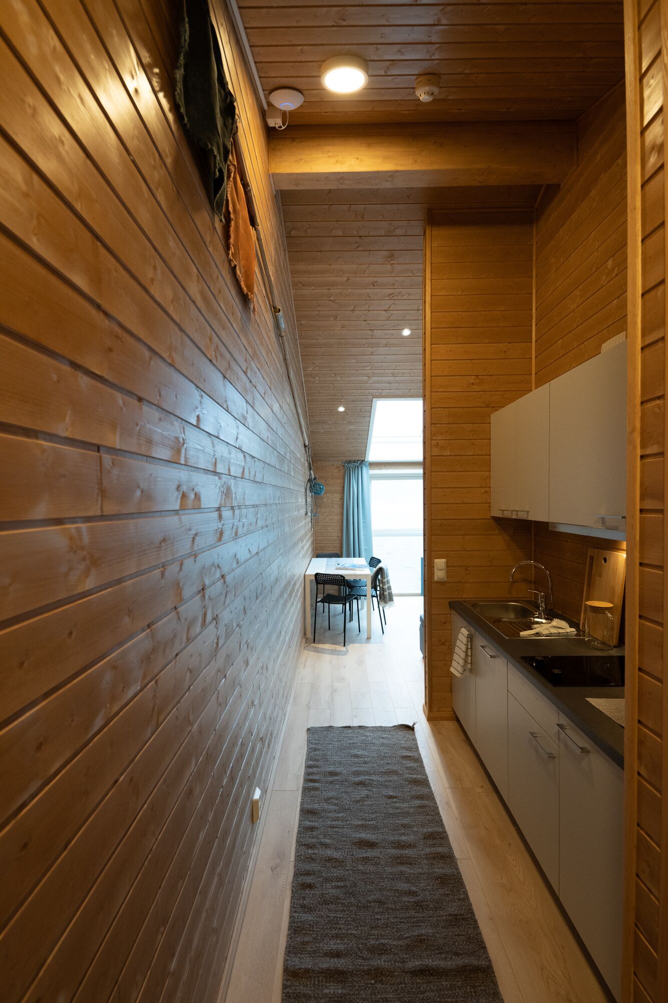 A narrow hallway with wooden walls and a kitchen area with a sink and cabinets.