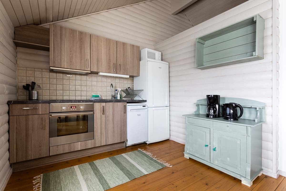 A compact kitchen with wooden cabinets, a white refrigerator, a coffee maker, and a striped rug.
