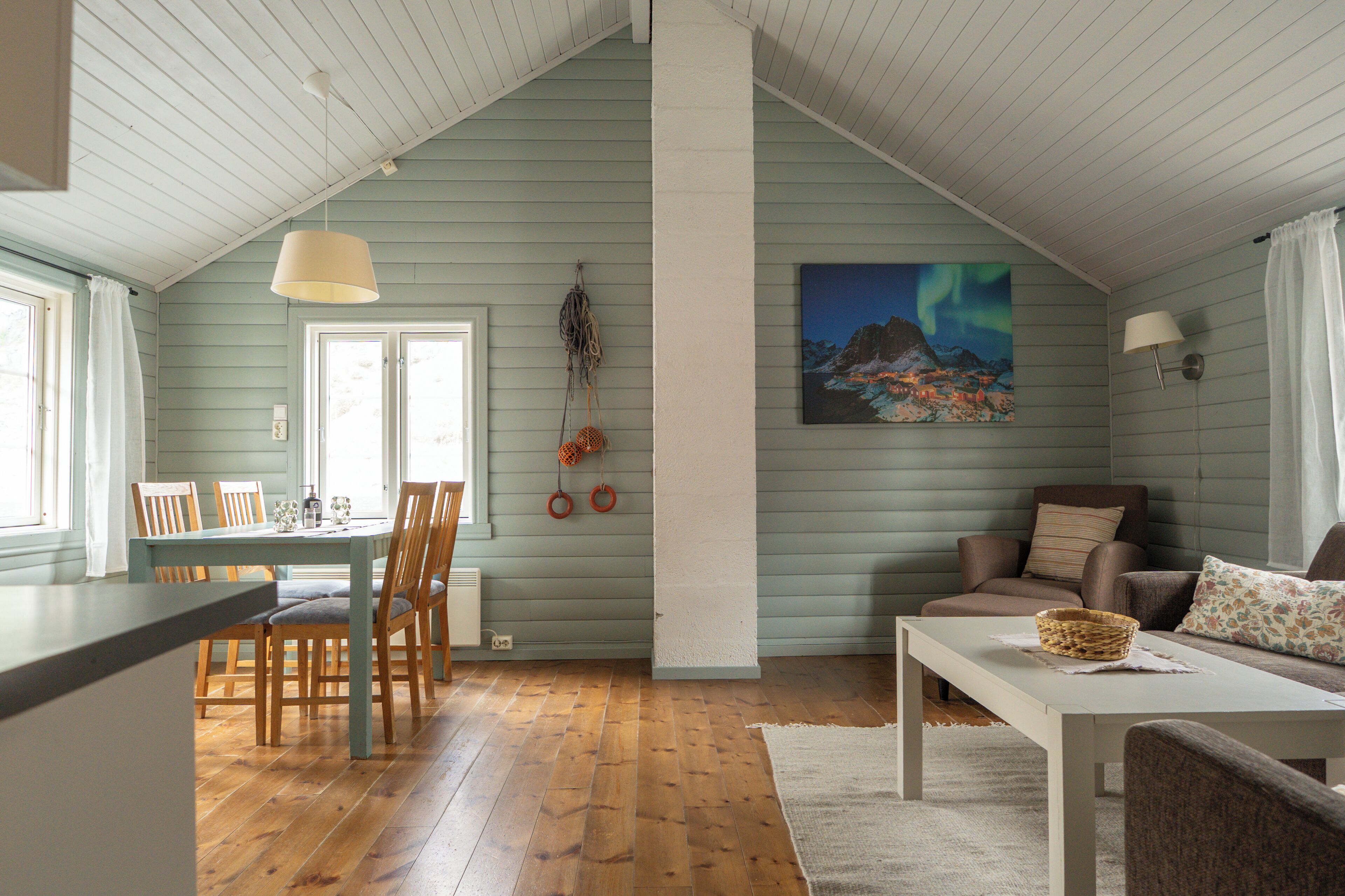 A cozy room with a dining area, a sofa, and a painting of the aurora borealis.