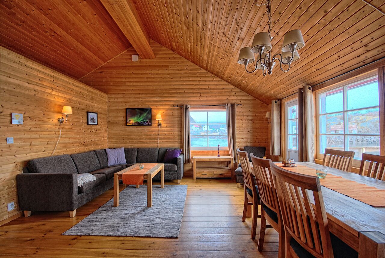 Interior acogedor de una cabaña de troncos con techo de madera, un sofá, una mesa de comedor con sillas y vistas a través de una ventana.