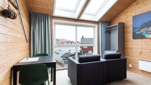 Tunnelmallinen huone, jossa on puusisustus, suuri ikkuna, josta avautuu näkymä merelle, musta sohva, pöytä ja tuoli sekä seinälle asennettu televisio.