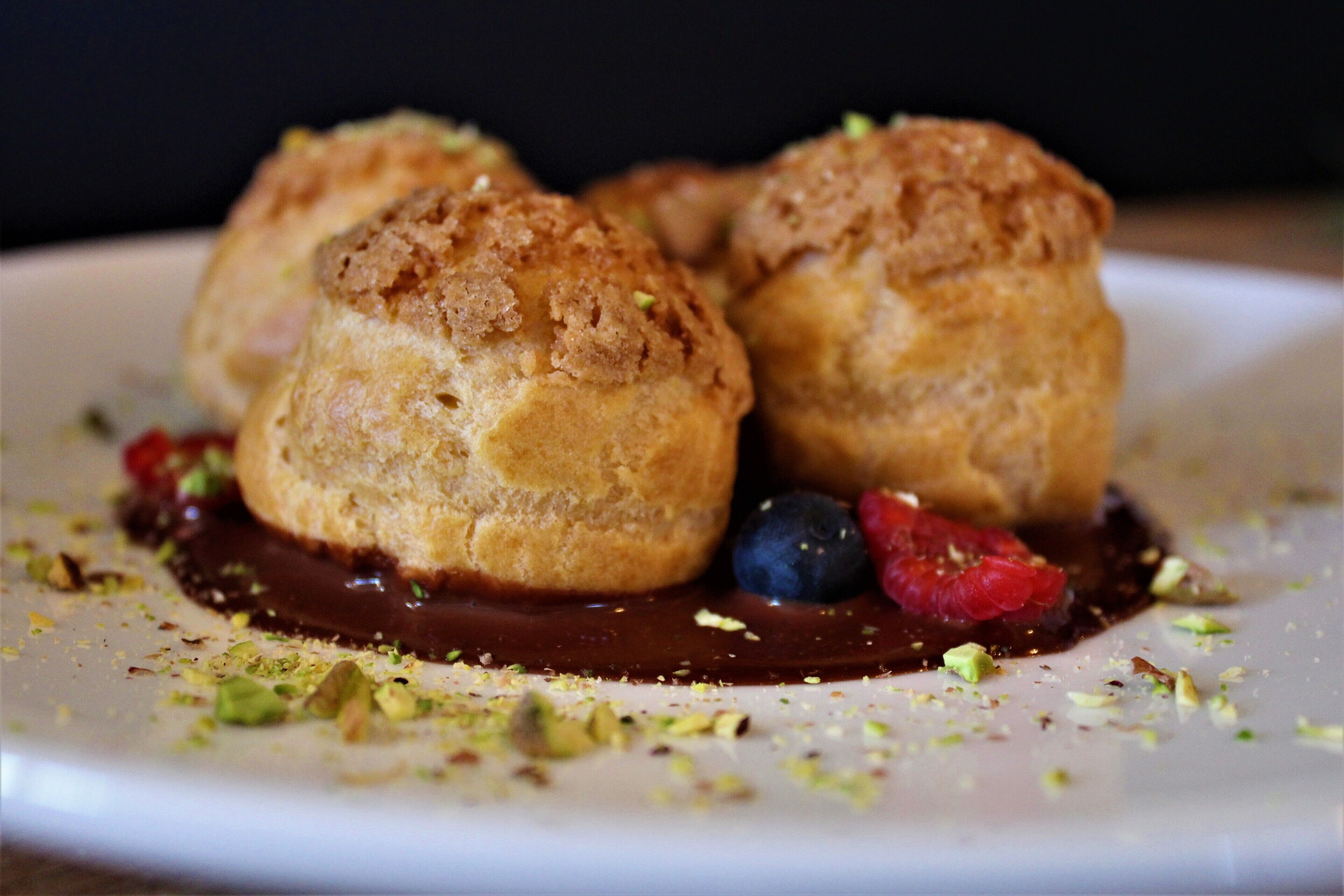 A dessert plate with three pastries, chocolate sauce, and scattered pistachios.