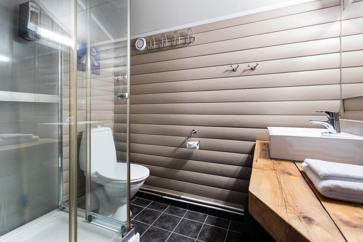 A bathroom with a glass shower enclosure, a toilet, a sink with a wooden vanity, and a towel rack on the wall.