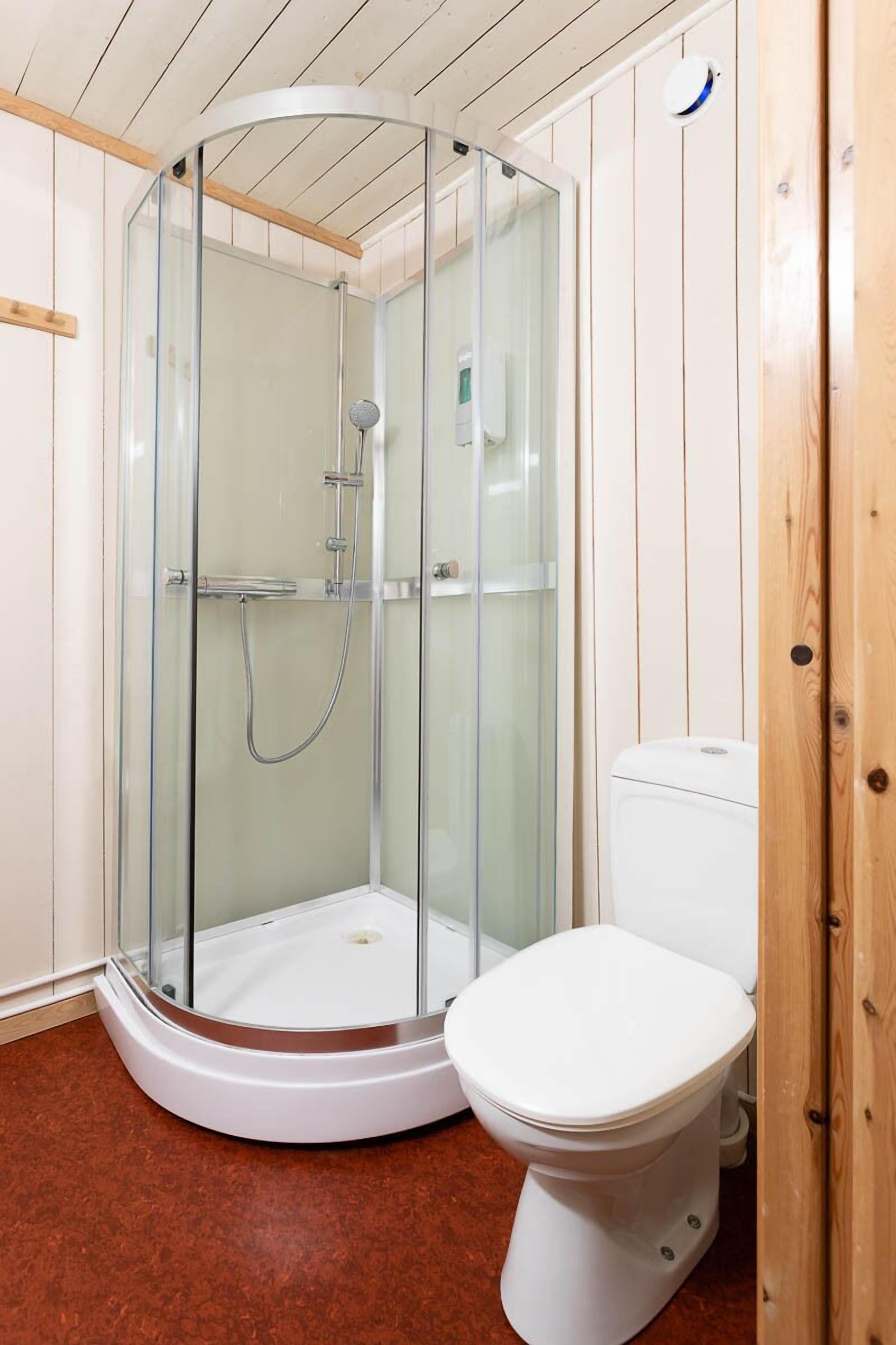 A bathroom with a glass-enclosed shower, a white toilet, and wooden paneling on the walls.