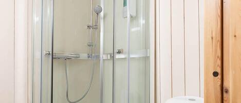 A bathroom with a glass-enclosed shower, a white toilet, and wooden paneling on the walls.