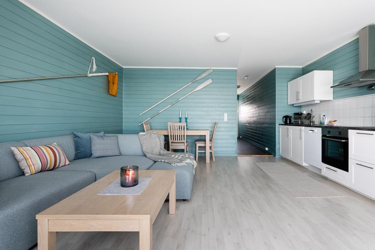 A modern living room with a teal-colored wall, a gray sofa, a wooden coffee table, and a dining area with a wooden table and chairs.