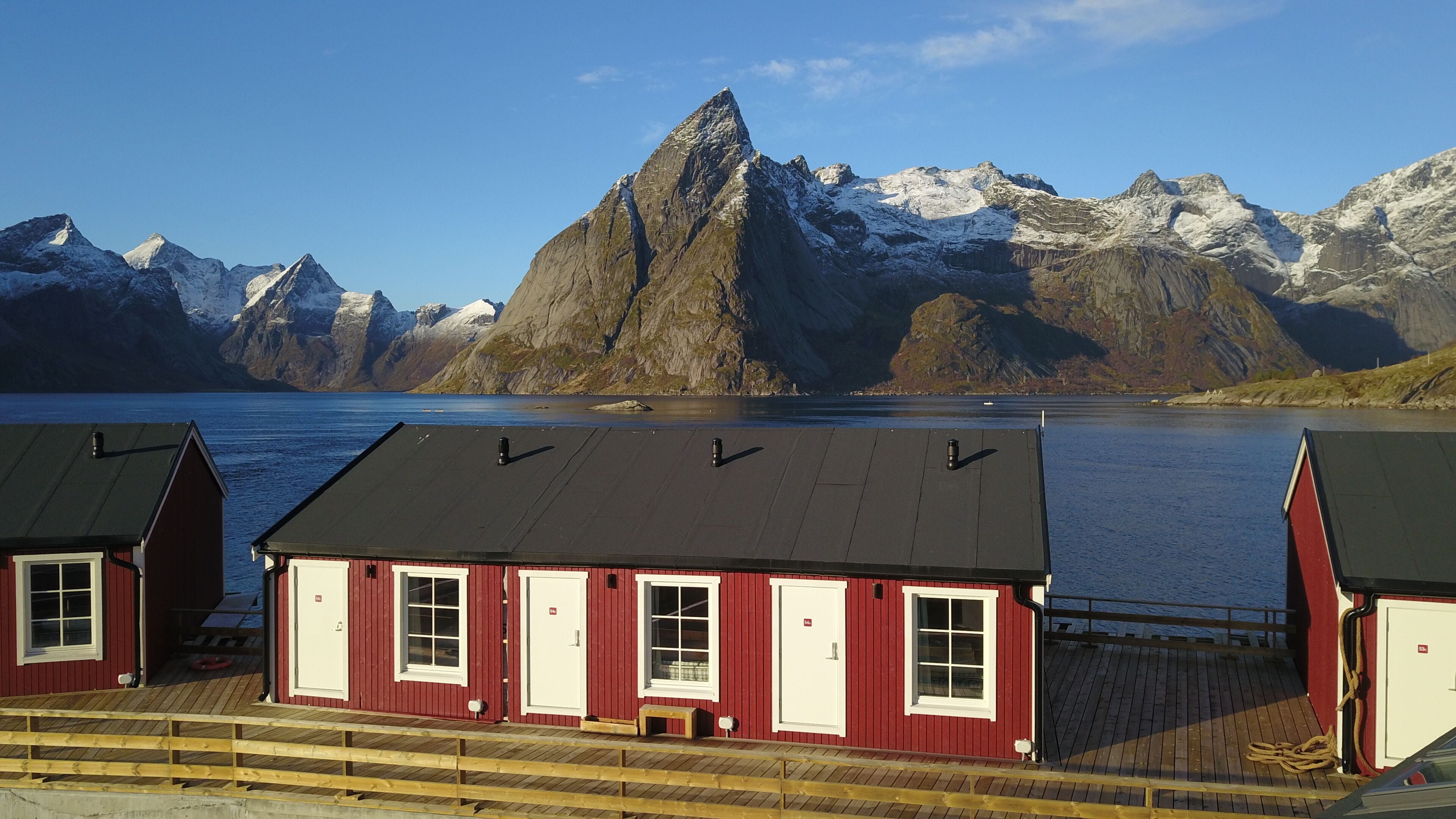 A row of red wooden cabins with black roofs, white windows, and a wooden deck in front.