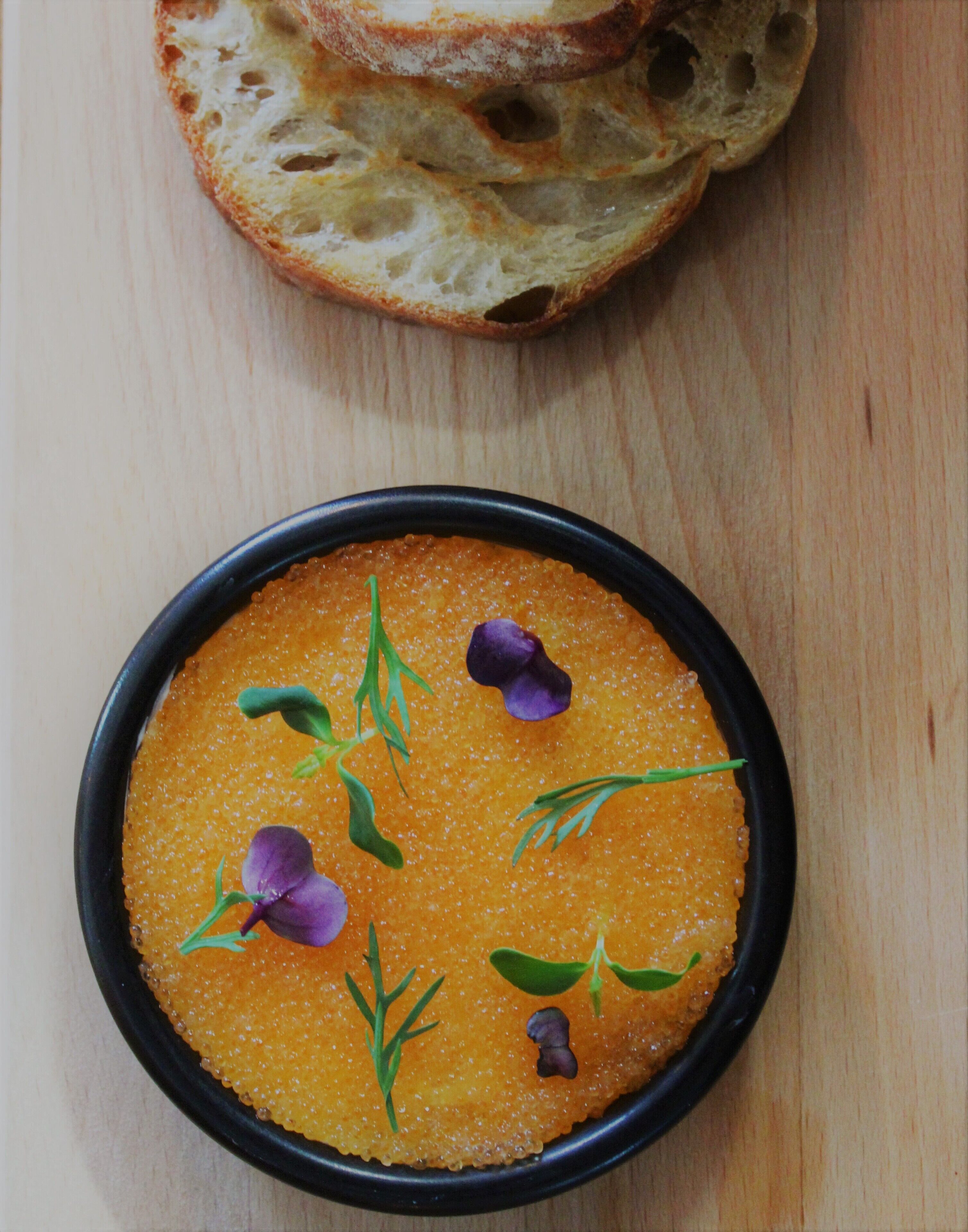 Eine Schüssel Orangensuppe, garniert mit Kräutern und Blumen, mit Brotscheiben auf einem Holztisch.