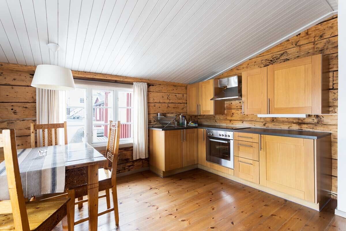 Een compacte keuken met houten keukenkastjes, een fornuis en een eethoek met een tafel en stoelen.