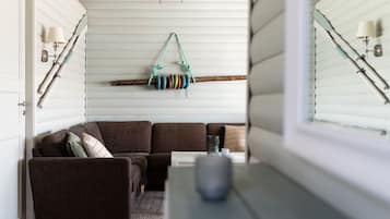 A cozy living room with a brown sectional sofa, a small rug, and a wooden coffee table. A colorful rope swing hangs from the ceiling, and a dreamcatcher is visible.