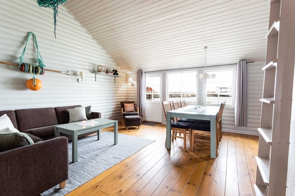 A cozy living room with a sofa, coffee table, and dining area with chairs. A window provides a view of the outside.