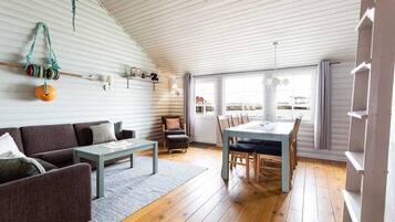 A cozy living room with a sofa, coffee table, and dining area with chairs. A window provides a view of the outside.