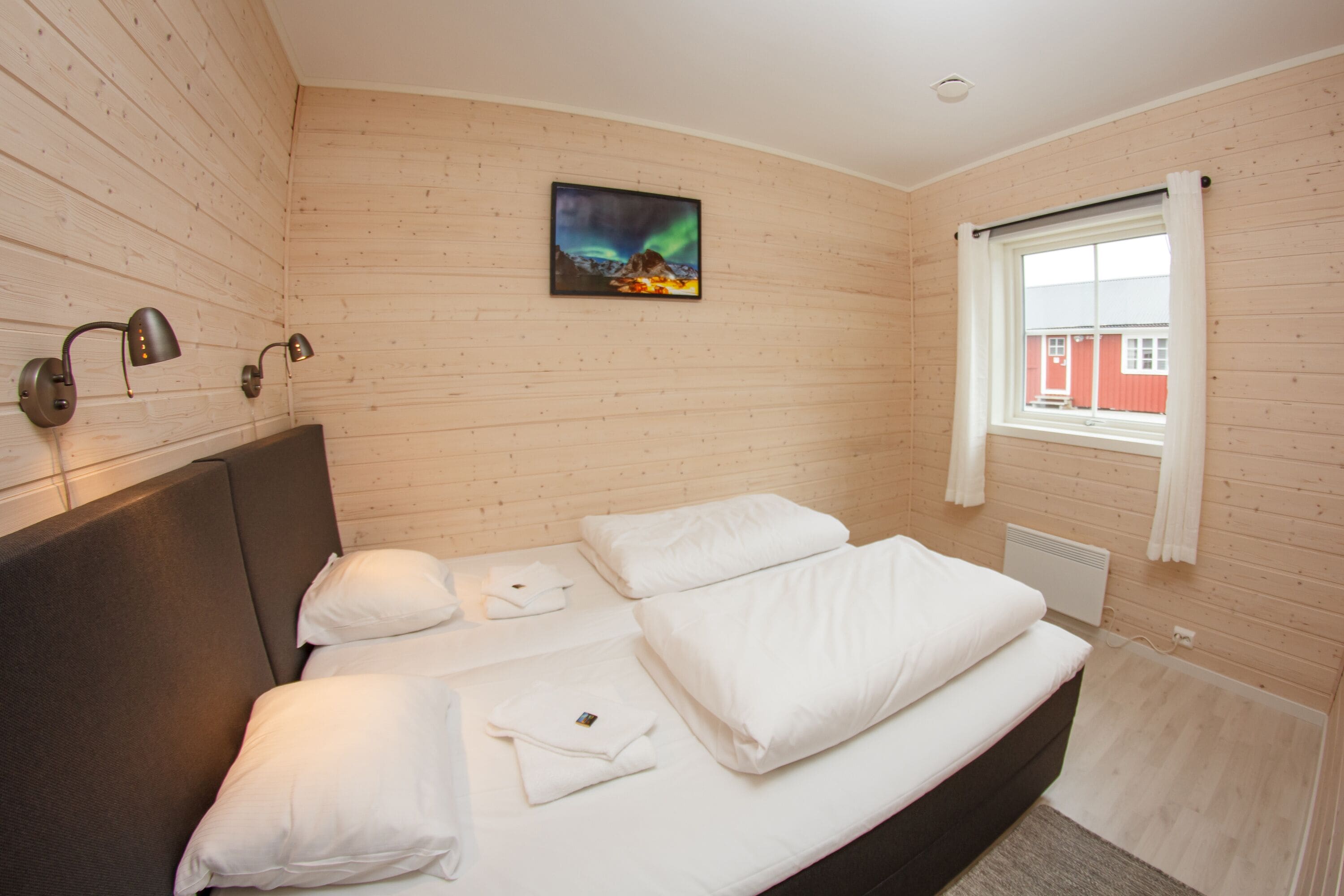 A neatly made bed with white linens, a headboard, and a painting of the aurora borealis on the wall.