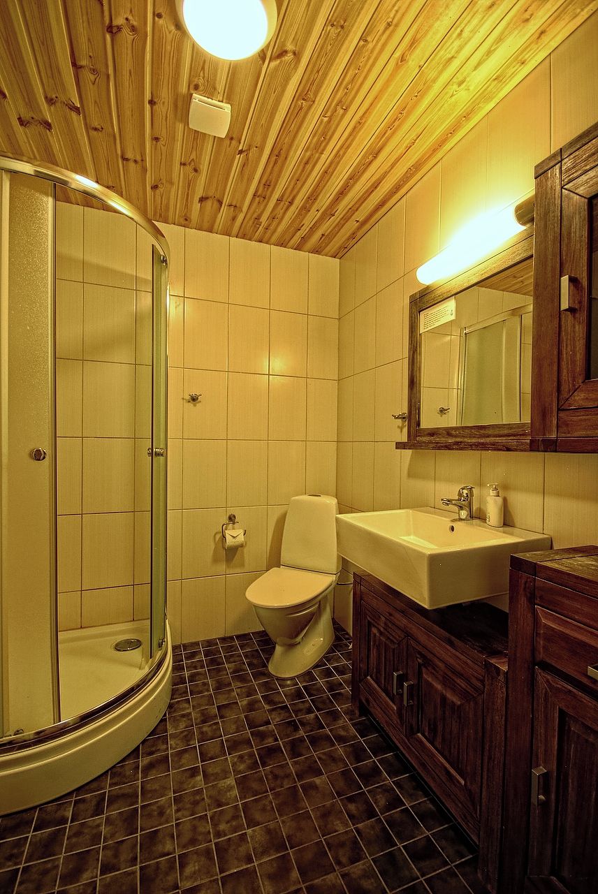 Un baño con ducha envuelta en vidrio, inodoro, lavamanos y armarios de madera.