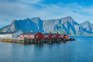 A row of red wooden houses on stilts over water, with a mountain range in the background.