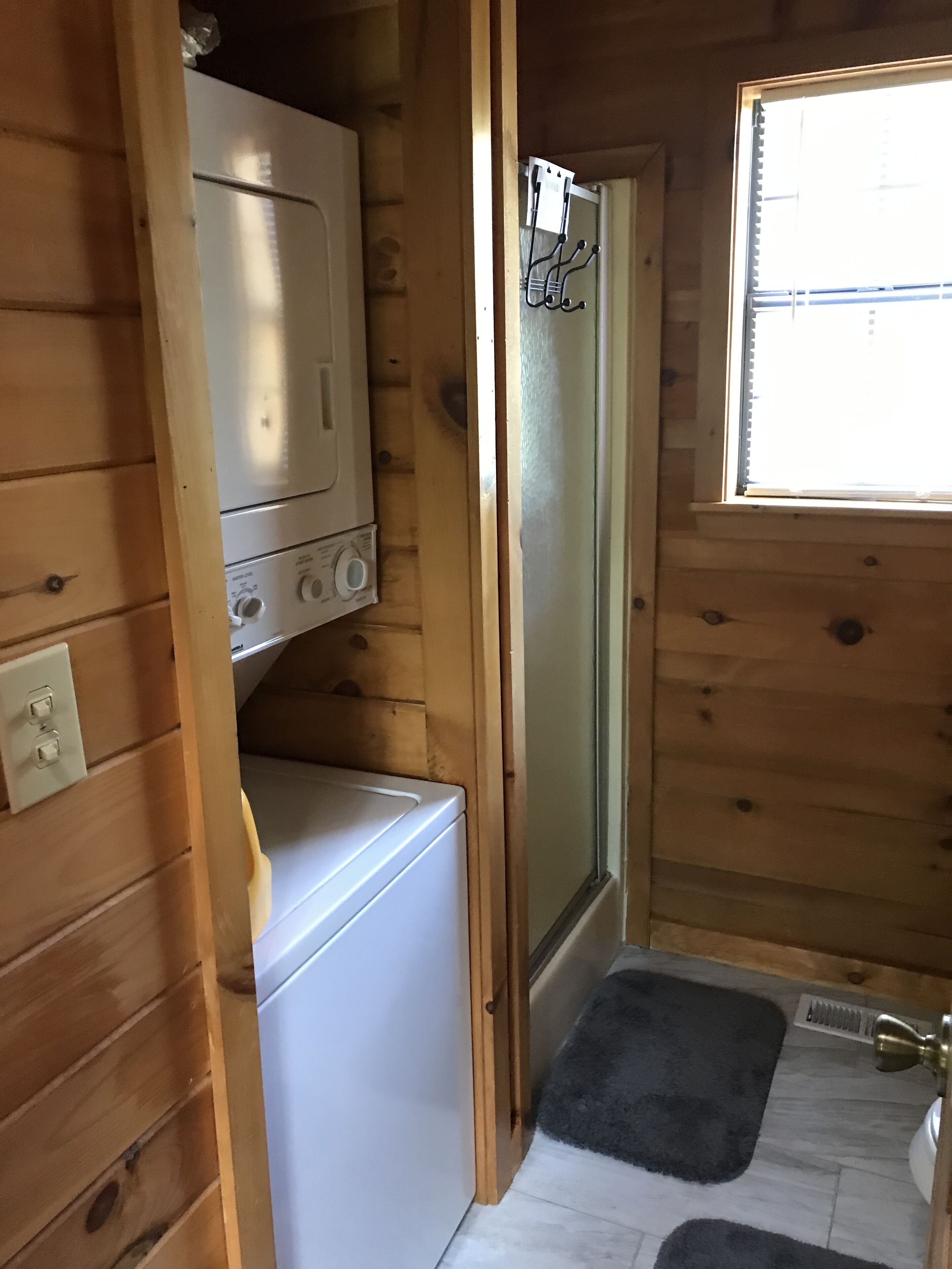 A compact wooden cabin with a washing machine, a small refrigerator, and a door with a frosted glass panel.