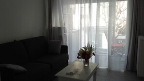 Ein Wohnzimmer mit einem dunklen Sofa, einem kleinen Tisch mit Blumenvase und transparenten Vorhängen.