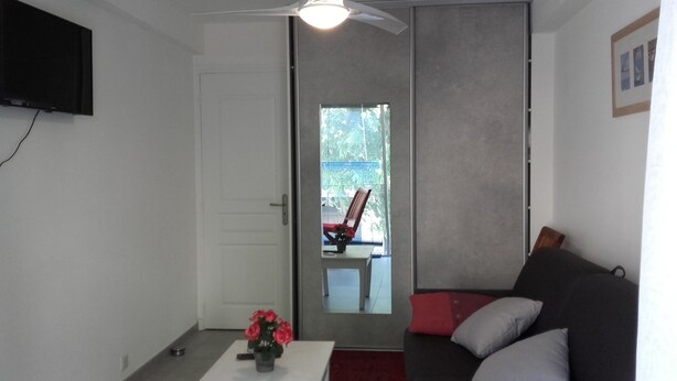 Ein Wohnzimmer mit einer Couch, einem Couchtisch mit Blumen, einem Fernseher und einer Schiebetür zu einem Außenbereich mit Stuhl und Tisch.
