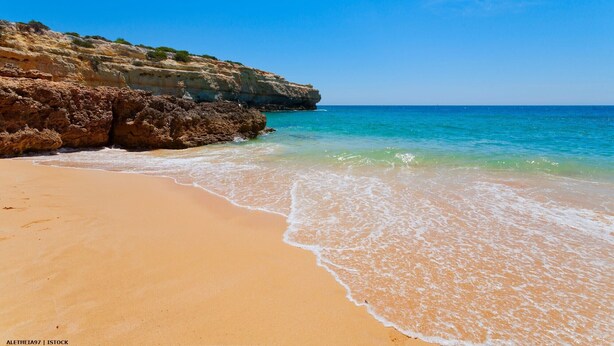 Una spiaggia con acque blu cristalline, una riva sabbiosa e scogliere rocciose.