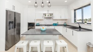Una cucina moderna con mobili bianchi, un'isola centrale con sgabelli, un frigorifero in acciaio inossidabile e luci a sospensione.