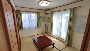 Ein Zimmer mit Tatami-Boden, einem Holztisch und grünen Vorhängen.