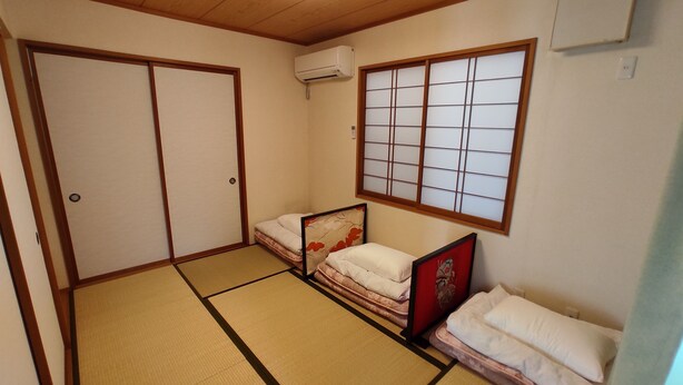 Ein traditioneller japanischer Raum mit Tatami-Boden, einer Schiebetür, einem Futonbett, einem Shoji-Bildschirm und einer Klimaanlage.