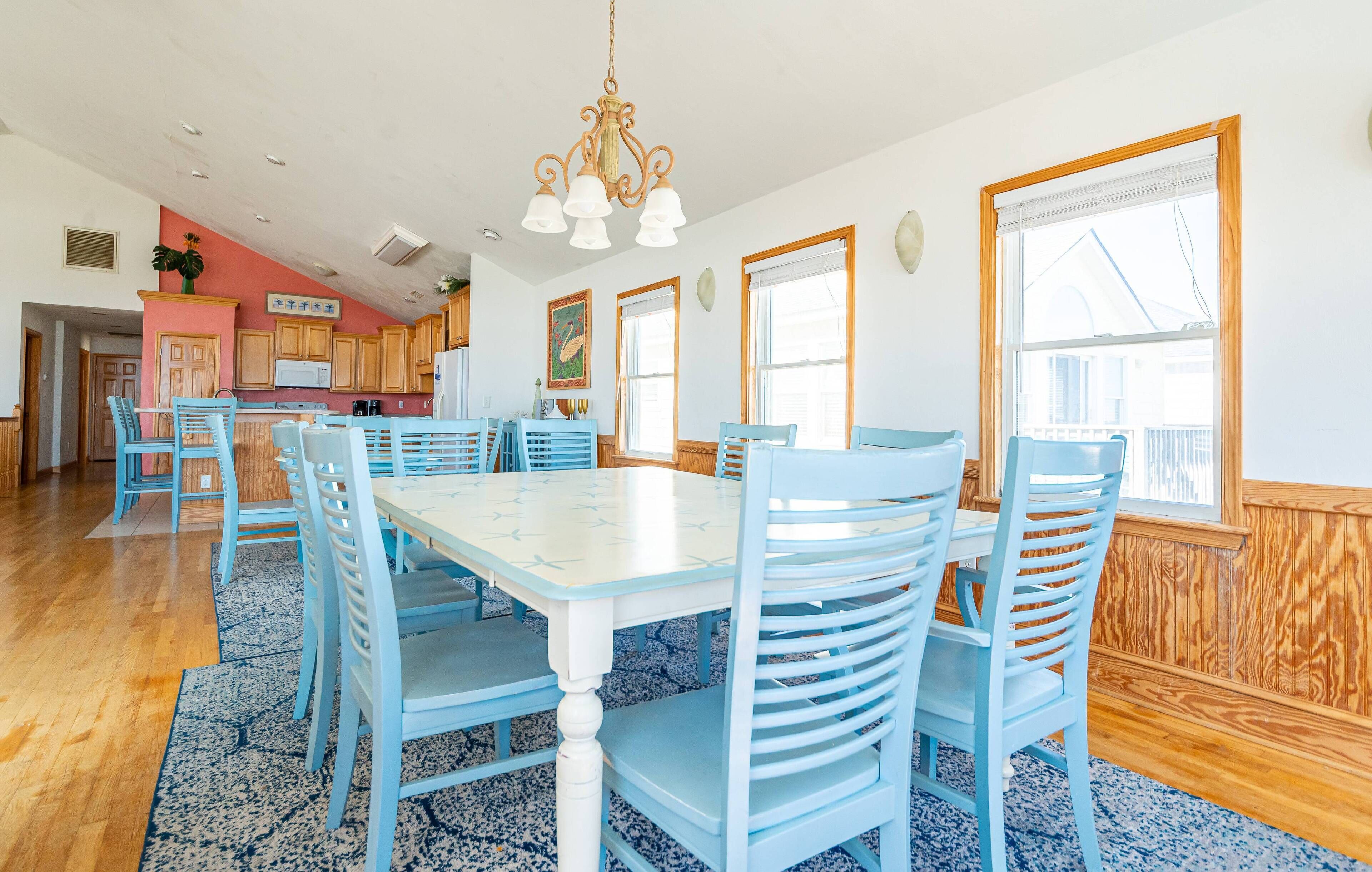 A spacious dining area with a large table and blue chairs, wooden cabinets, and a kitchen in the background.
