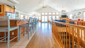 A spacious living area with a wooden staircase, a kitchen with wooden cabinets, and a large window providing natural light.