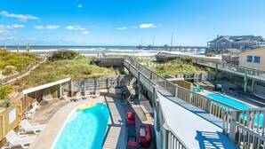 A pool area with a view of the beach and ocean, wooden deck, and lounge chairs.
