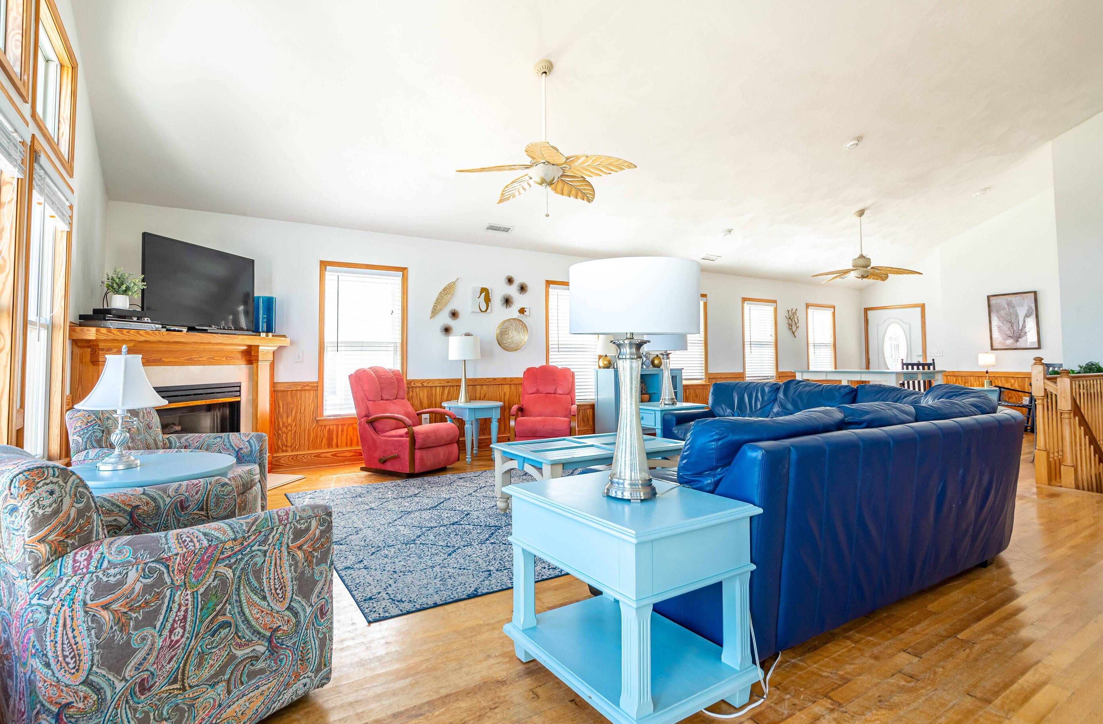 Ein geräumiges Wohnzimmer mit einem blauen Sofa, gemusterten Sesseln, einem Couchtisch und einem Kamin.