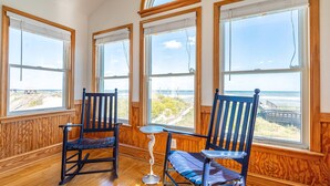 A room with wooden paneled walls, large windows with ocean views, two rocking chairs, and a small table.