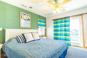 A bedroom with a large bed, a ceiling fan, a window with curtains, and a painting on the wall.