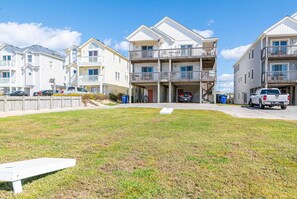A beachfront residential area with multi-story buildings, a grassy lawn, and parked vehicles.