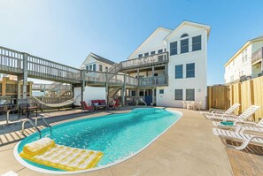 A pool area with a floating lounge, outdoor seating, and a multi-story building with balconies.