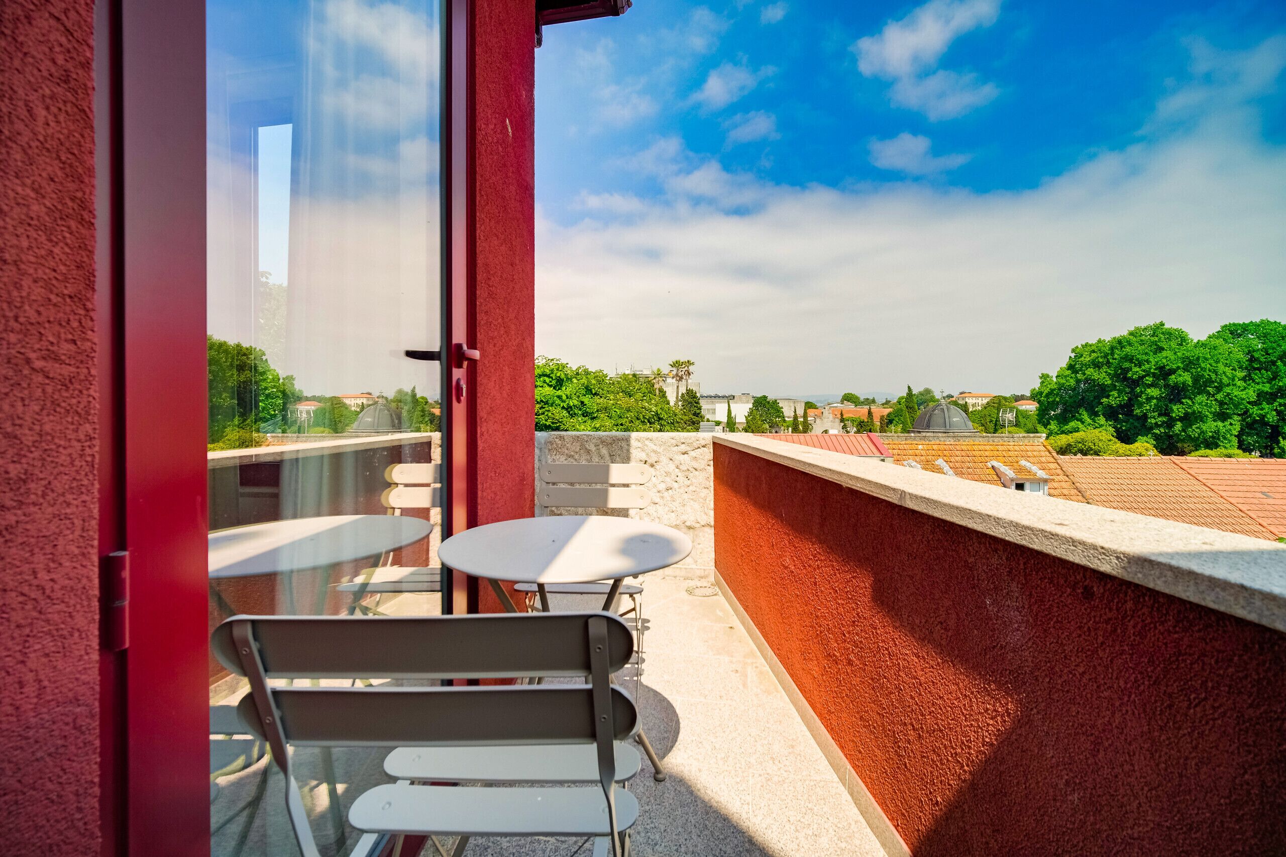 Un balcone con una porta vetrata, due tavoli bianchi e una panca.