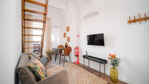 A living room with a sofa, a coffee table, a TV mounted on the wall, a wooden ladder, and a small table with a vase of flowers. - Nomads Nest in Bonfim 1BED Balcony View (Porto)
