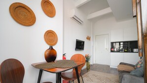 A modern living room with a dining area, featuring a round table, wooden chairs, a sofa, and a kitchen in the background. - Nomads Nest in Bonfim 1BED Balcony View (Porto)